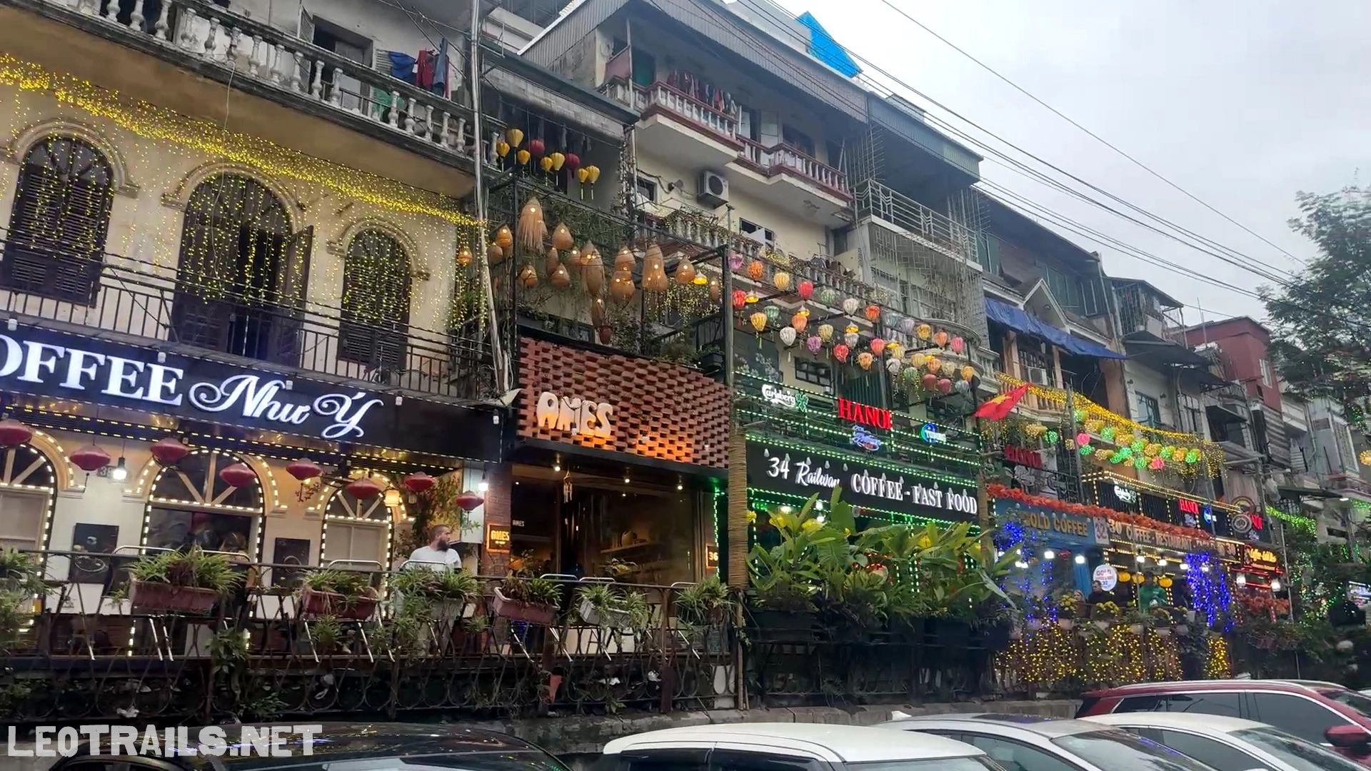 A row of multi-story cafes with glowing neon signs and colorful lanterns overlooking the train tracks at Hanoi Train Street in Vietnam.