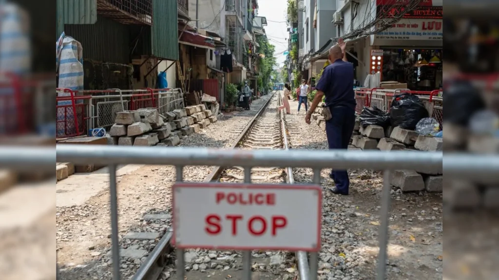 A metal barricade with a red and white sign reading "POLICE STOP" blocking entry to a straight section of the railway tracks at Hanoi Train Street