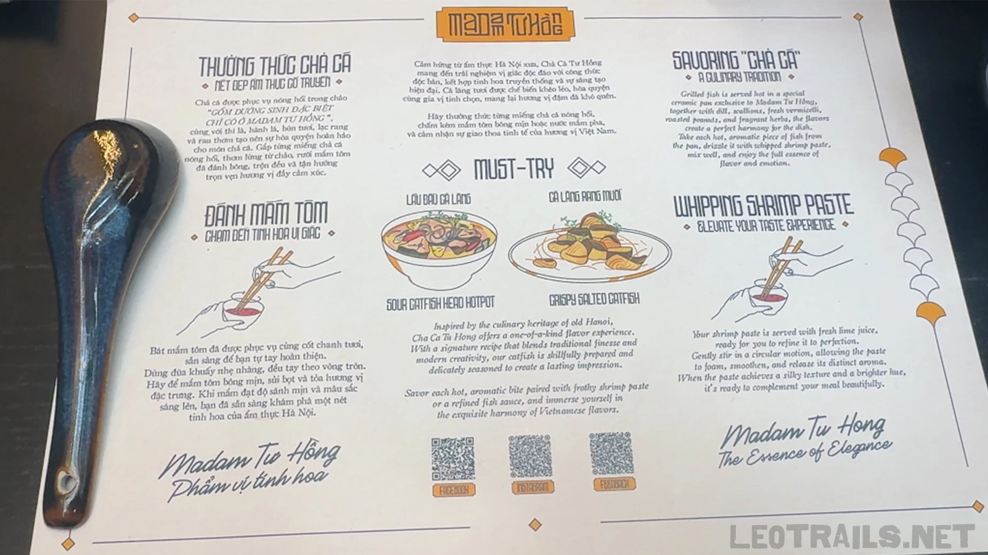 A detailed table placemat at Madam Tuấn (Madam Tu Hong) explaining how to savor Chả Cá and whip shrimp paste, with a blue ceramic spoon resting on the left side.