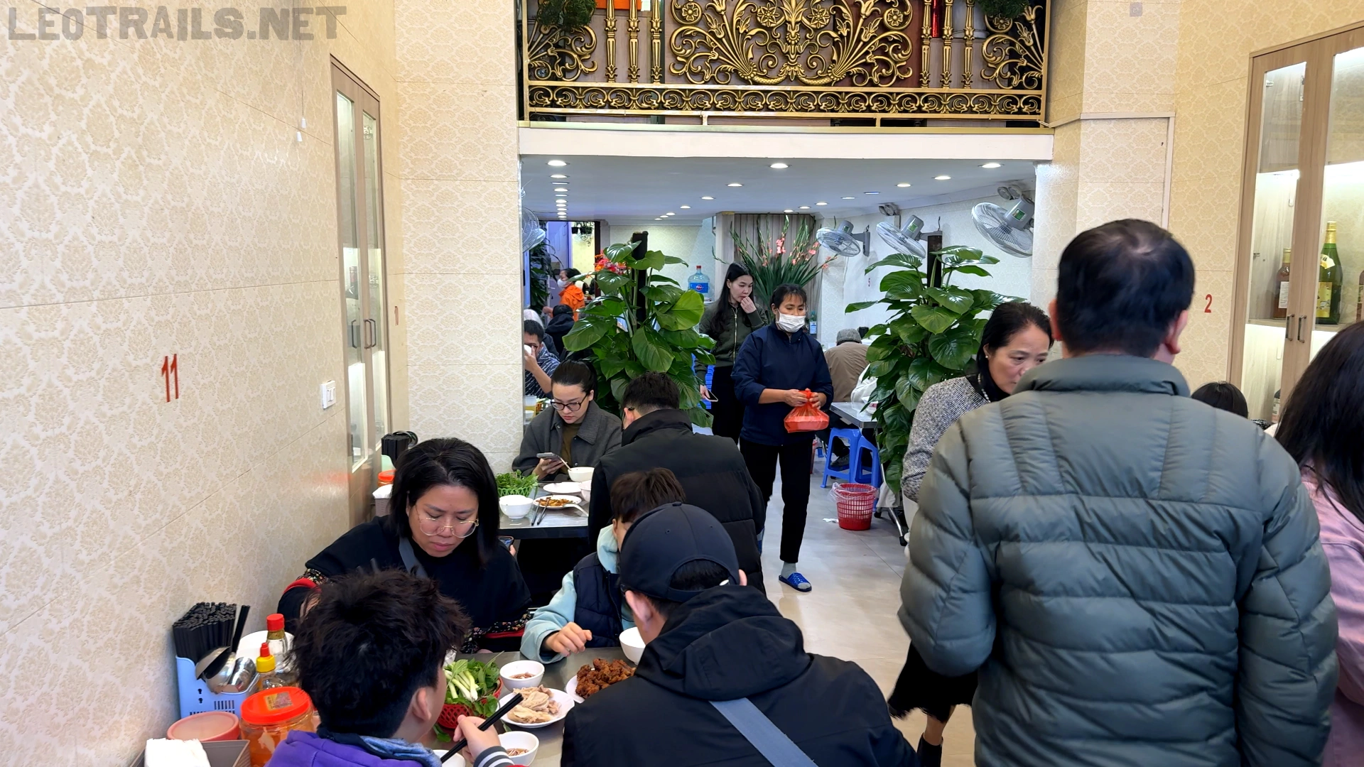 The crowded indoor dining room of the Bún Miến Ngan restaurant on Lý Nam Đế, filled with customers sitting at tables and a waitress carrying a dish in the background.