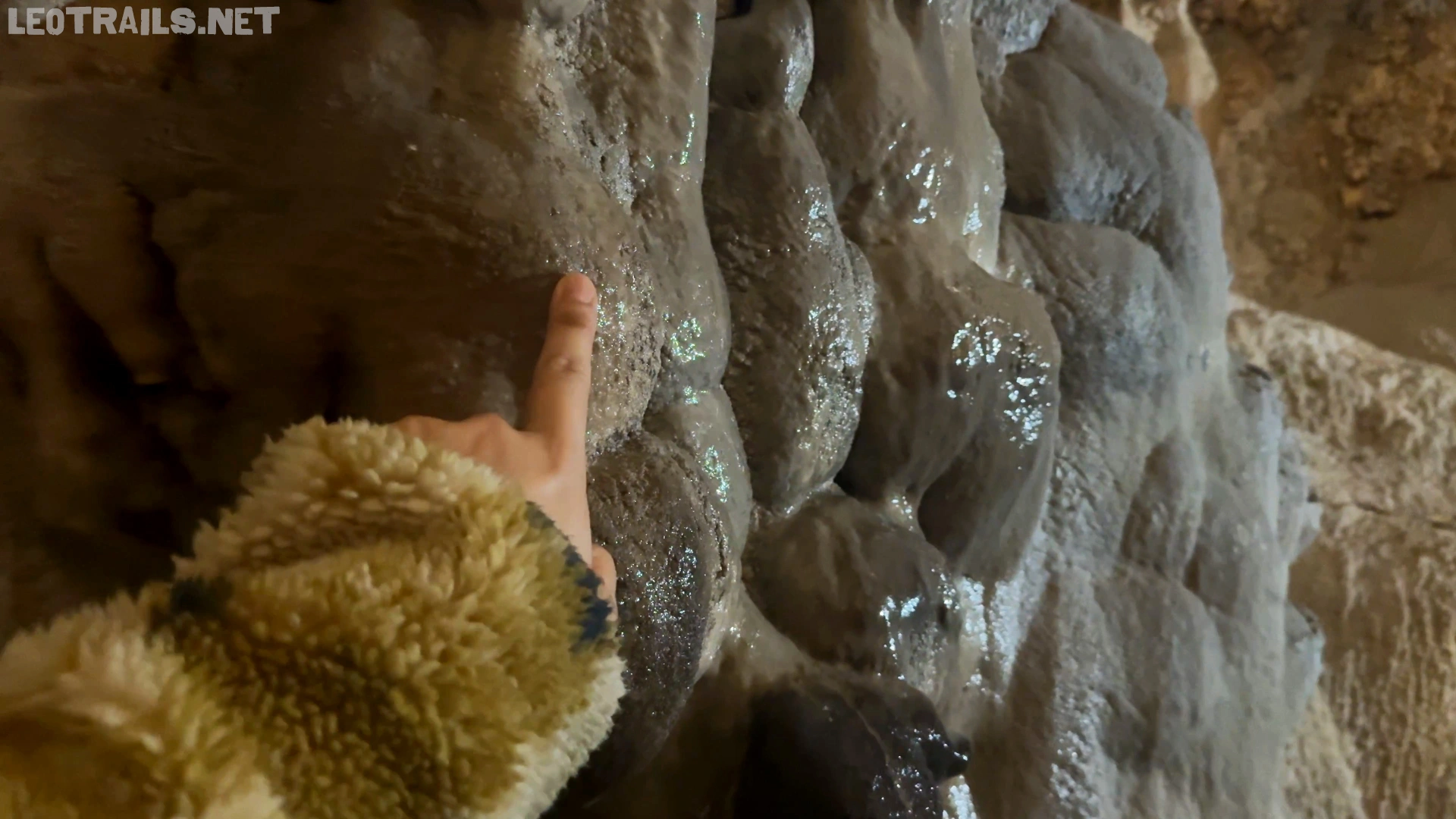 Close-up view of a person pointing at a wet, bumpy, gray limestone rock formation inside a cave.