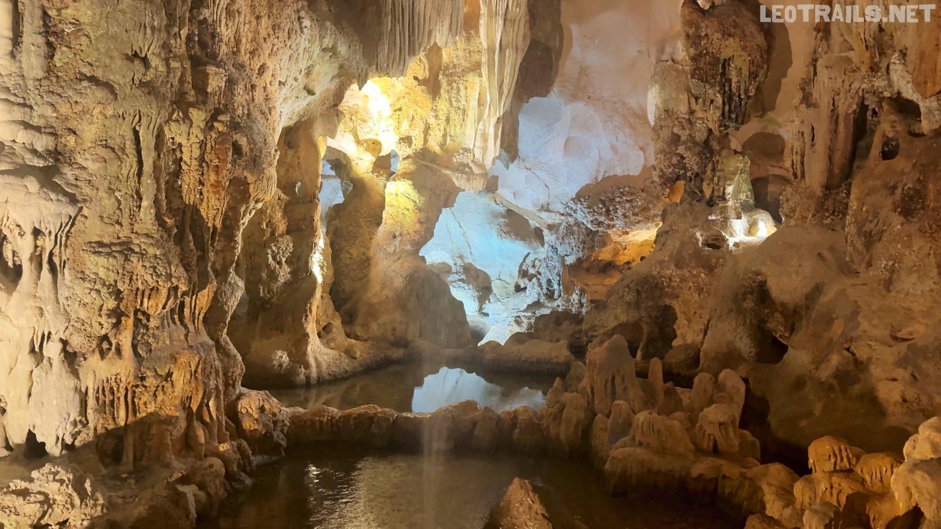 A hidden underground oasis featuring a quiet reflection pool surrounded by pillars of stone A serene, natural water pool reflecting the illuminated limestone pillars and flowstones deep inside Thien Cung Cave.A serene, natural water pool reflecting the illuminated limestone pillars and flowstones deep inside Thien Cung Cave.