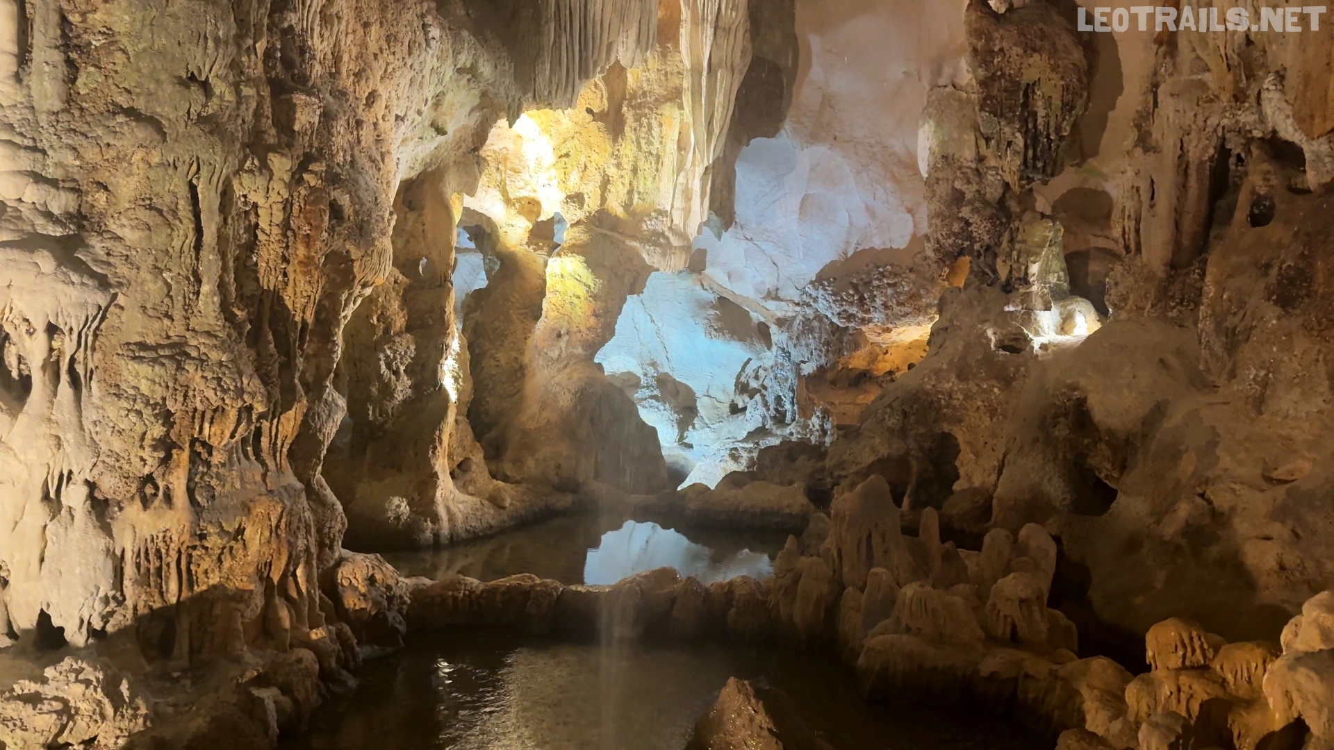 A serene, natural water pool reflecting the illuminated limestone pillars and flowstones deep inside Thien Cung Cave.